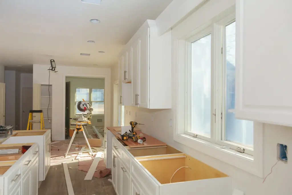 White kitchen cabinets installed without countertops, with a miter saw, cordless drills, and ladder in a home under